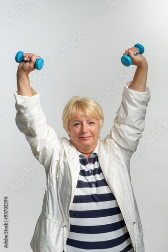 Mature woman doing physical exercises with dumbbells in sportswear