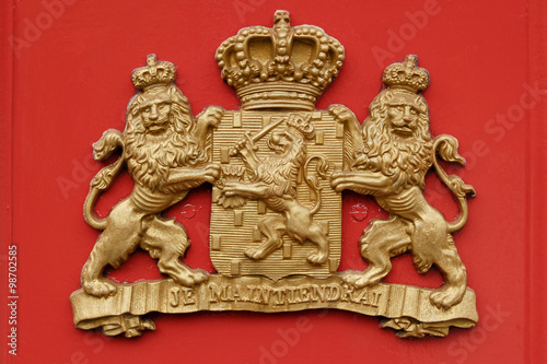 A coat of arms  showing two lions holding a shield with a third lion on it and a crown. The motto Je Maintiendrai is the motto of the House of Orange and Nassau, the Royal Family of the Netherlands.