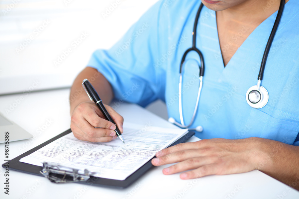 Portrait of unknown male surgeon doctor holding his stethoscope and filling up medical prescription Portrait of unknown male surgeon doctor holding his stethoscope and filling up medical prescription