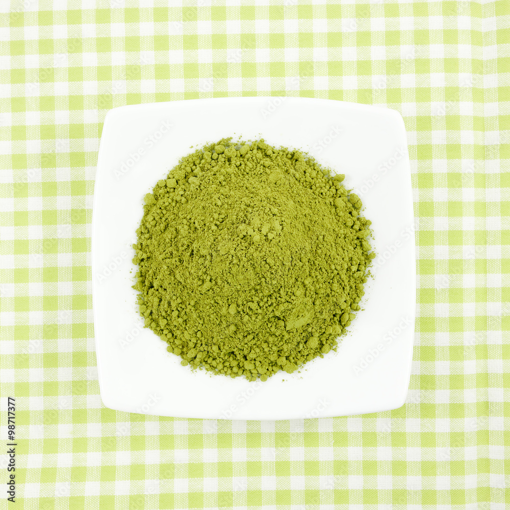The Japanese matcha green tea powder on the mini white dish on green cotton fabric. The Japanese matcha green tea powder on the mini white dish on green cotton fabric.