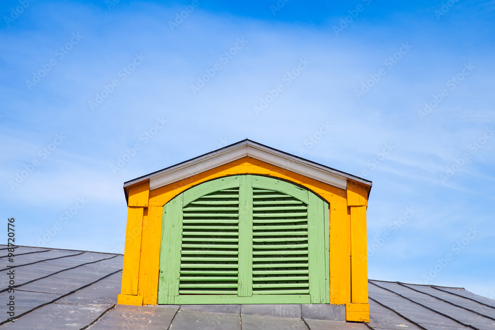 Yellow wooden attic window with green shutters