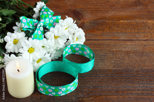 a bouquet of white daisies with ribbon and candle on wooden table