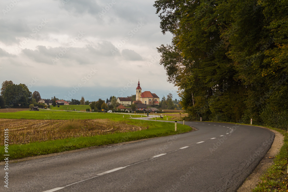 Rural asphalt road and the church between villages Skarucna and Vojsko in Slovenia.