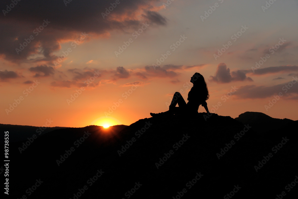 Silhouette of a girl sitting on a hill against the setting sun