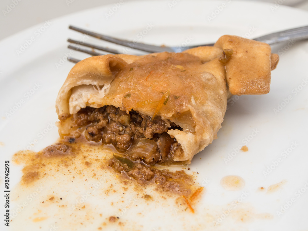 Half eaten empanada on a white plate with a fork hidden behind Half eaten empanada on a white plate with a fork hidden behind
