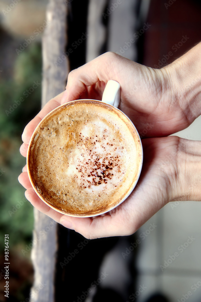 Cup of tasty cappuccino with hands on street background Cup of tasty cappuccino with hands on street background