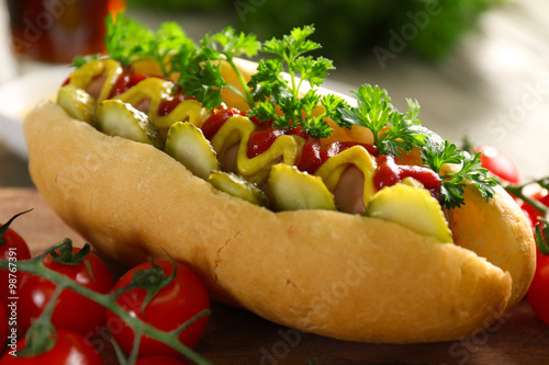 фотографія Delicious hot-dog with tomatoes and ketchup on wooden chopping board, close up