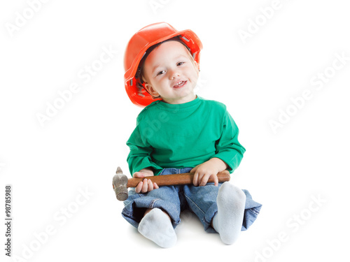 Little child plays with hammer and orange construction protective helmet on white background.