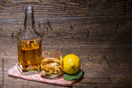 Bottle with a glass with whiskey and lemon are on the napkin