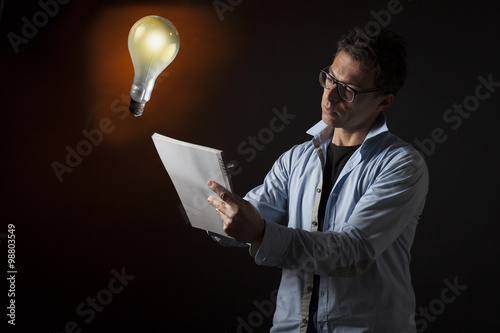 Concetto di ingegno, idea e creatività : uomo d'affari scrive su un quaderno. Sfondo con lampadina accesa