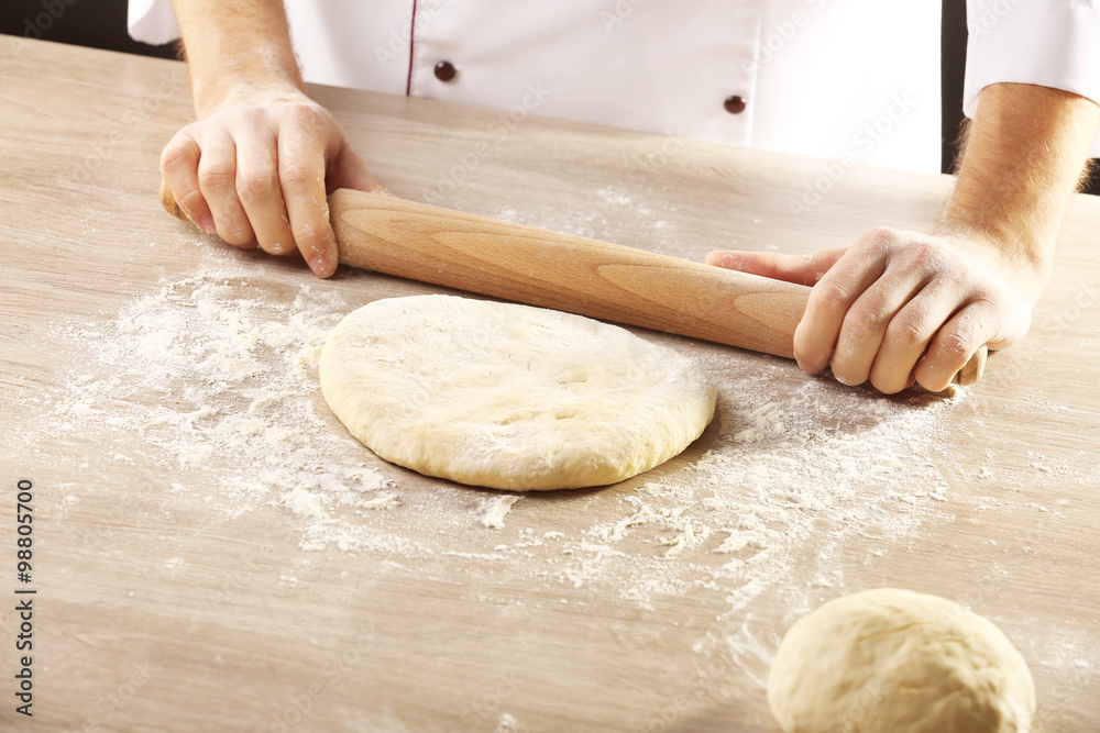 Hands rolling dough for pizza on the wooden table, close-up Hands rolling dough for pizza on the wooden table, close-up