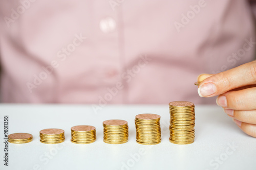 Female hand stacking gold coins into increasing columns