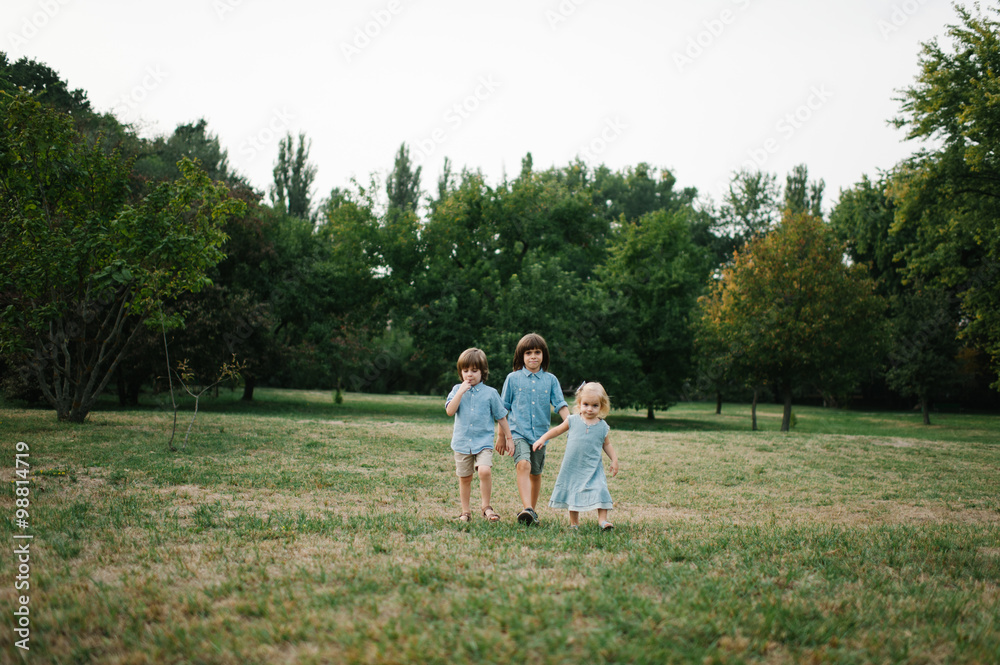 Three kids walking on grass in park on summer afternoon in park and playing to each other Three kids walking on grass in park on summer afternoon in park and playing to each other