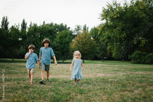 Three kids walking on grass in park on summer afternoon in park and playing to each other