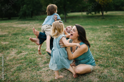 Happy young hipster family having fun while running, bowl, rising up, piggyback ride their children in park on summer sunset
