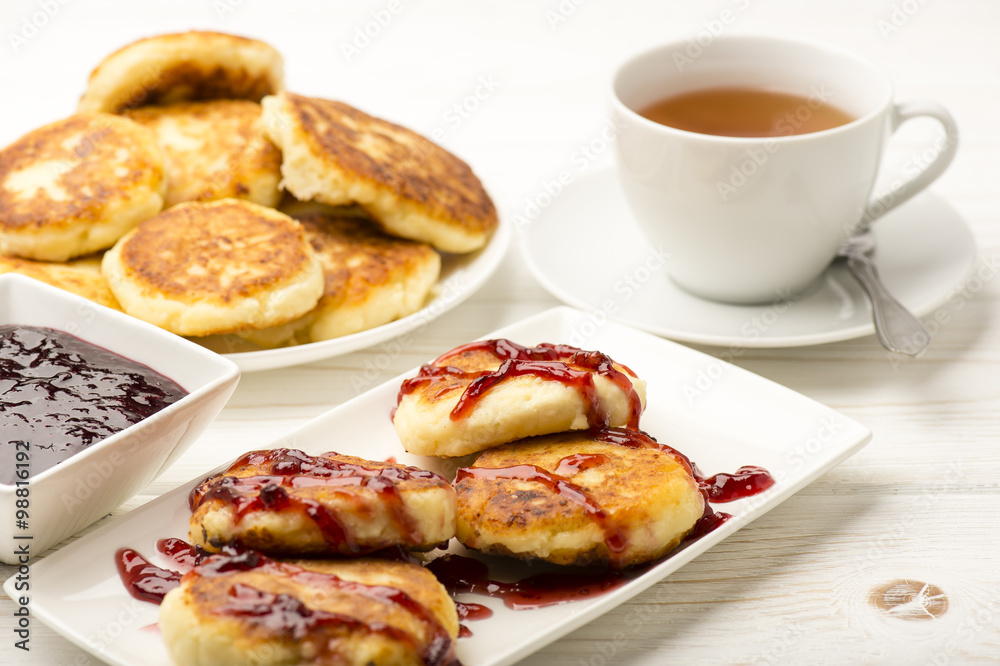 Cottage cheese pancakes with a cup of tea on the white wooden background.