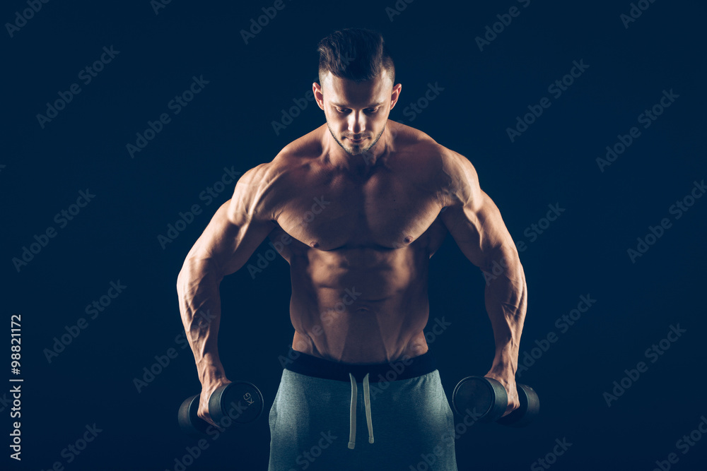 Fototapeta premium Closeup of a muscular young man lifting dumbbells weights on dark background