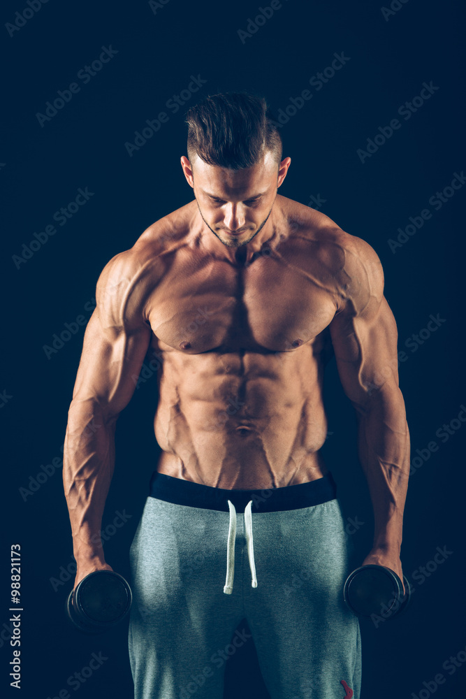 Fototapeta premium Closeup of a muscular young man lifting dumbbells weights on dark background