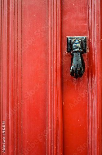Antique iron hand used to knocked on a red door