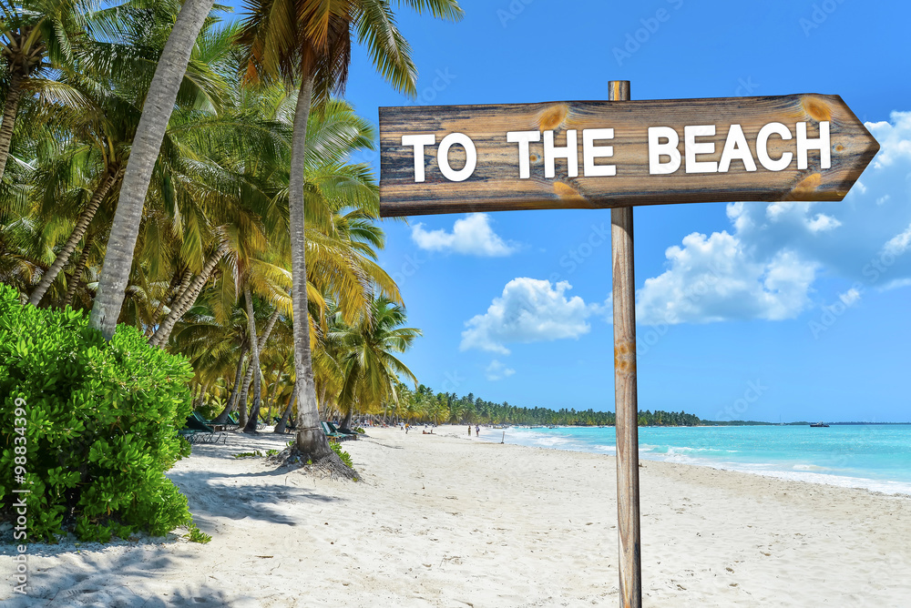 Beach Wood Sign with text To The Beach, Palm Trees, Tropical See and Blue Sky