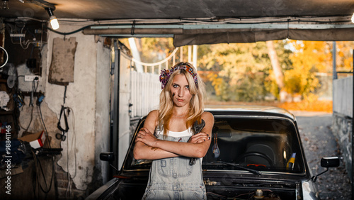 young blonde girl with long hair is an auto mechanic in the garage with a lot of tools on the shelves holding wrenches