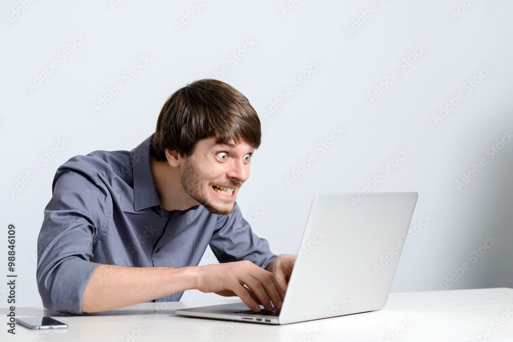 Feeling sick and tired. Frustrated young man holding head in hands and looking at laptop while working late at his working place Feeling sick and tired. Frustrated young man holding head in hands and looking at laptop while working late at his working place