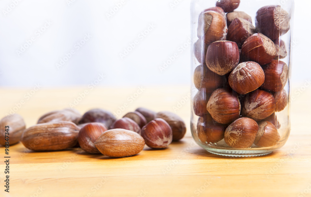 Pecan walnuts and hazelnut on glass jar over wooden surface