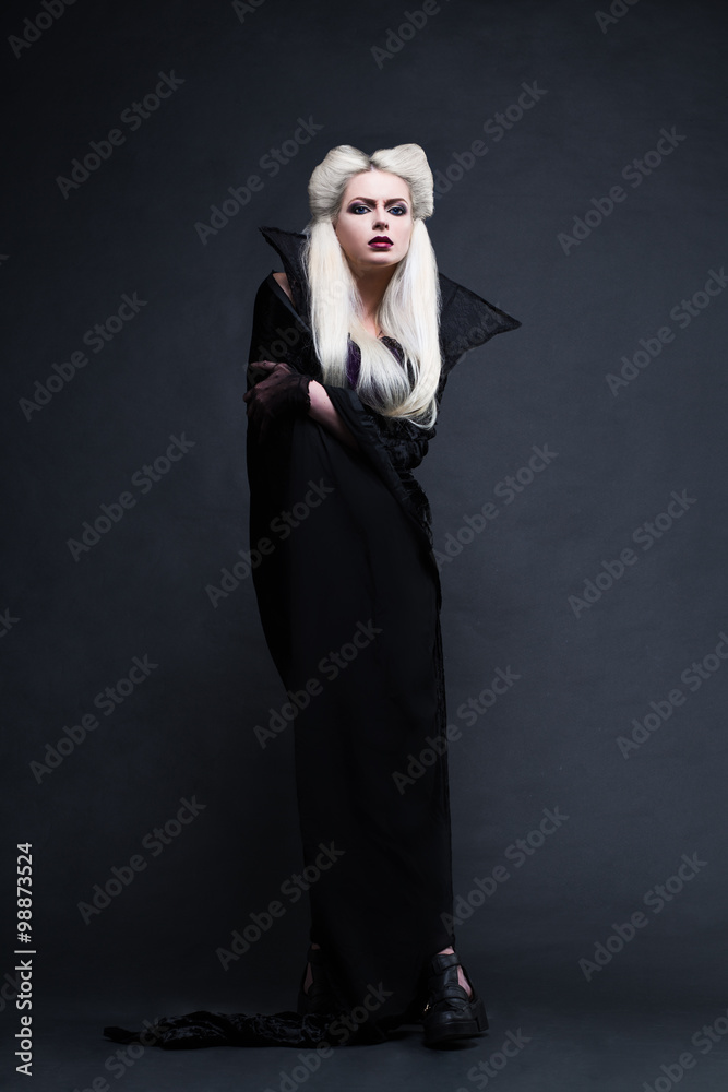 Beautiful blonde girl vampire standing. Studio photo with black background.
