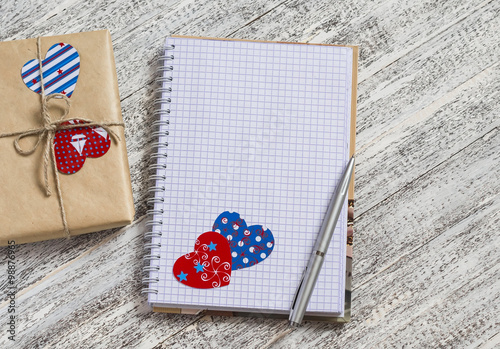 Open clean Notepad, homemade Valentine's day gifts in kraft paper, paper hearts on white wooden table. Vintage style