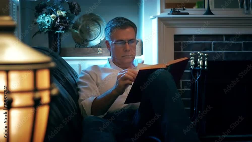 man reclining on his couch reading a book