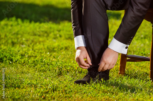 image of man in black suit putting on shoe at green grass