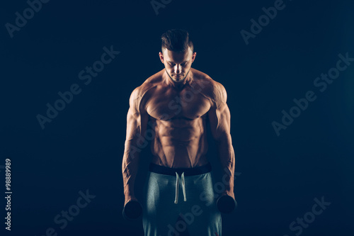 Closeup of a muscular young man lifting dumbbells weights on dark background