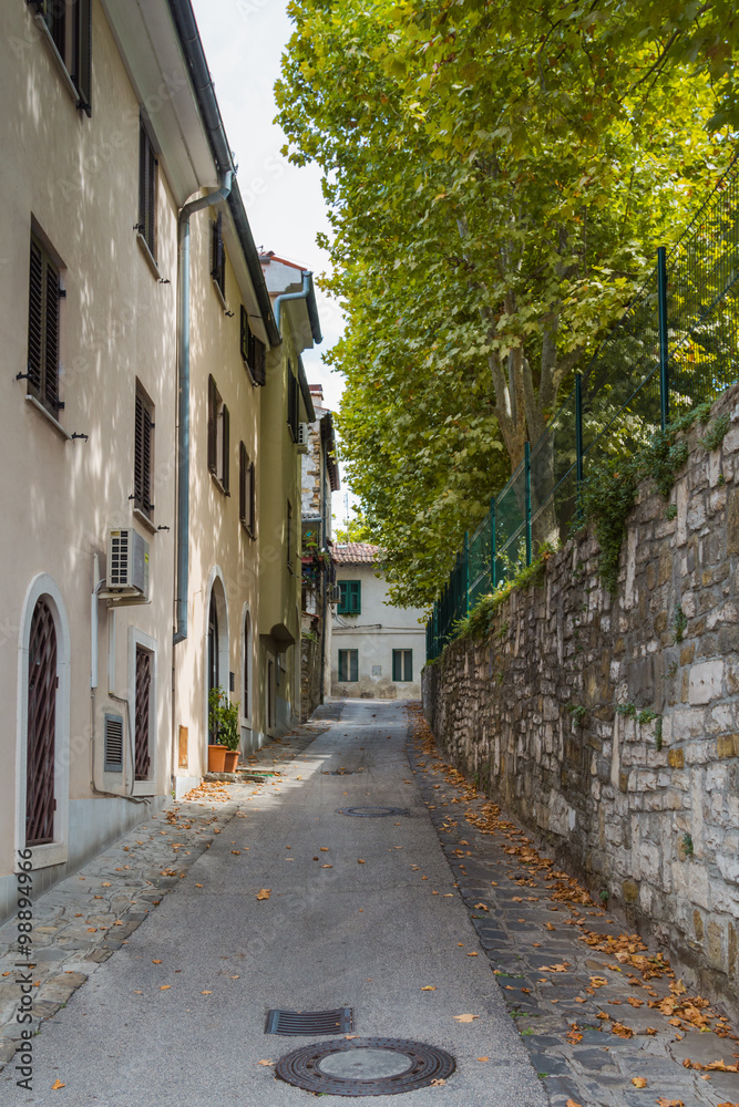 Narrow deserted small European street with houses on one side and stone wall on the other.