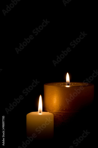 Two burning candles isolated on black background.