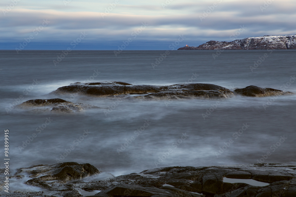 Stone beach and the lighthouse on the cape. Barencevo sea. Kola Peninsula. Murmansk region. Russia. Stone beach and the lighthouse on the cape. Barencevo sea. Kola Peninsula. Murmansk region. Russia.