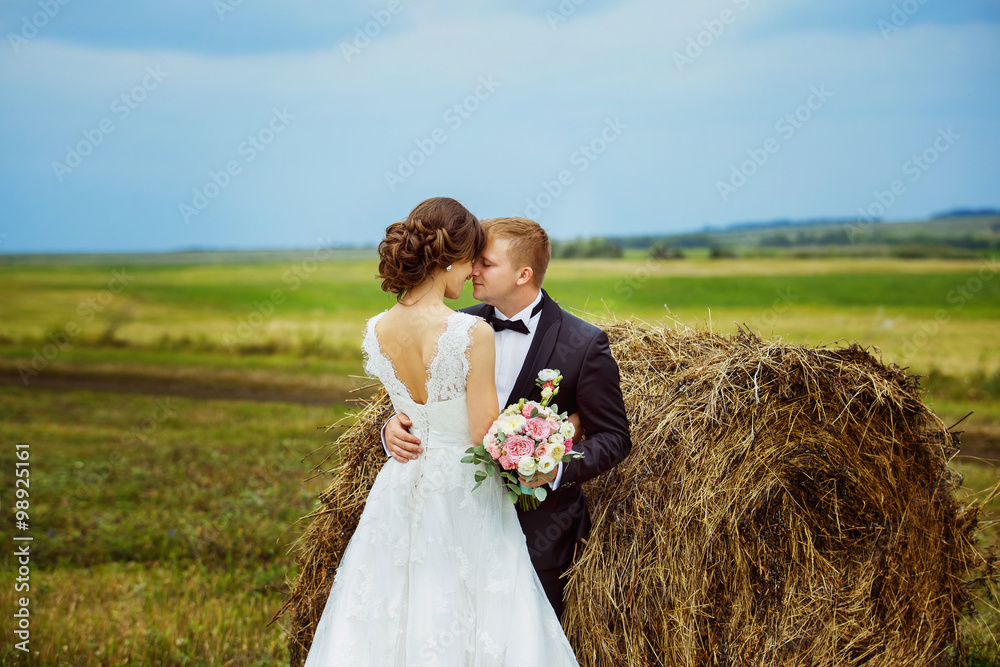 Beautiful young bride is tenderly embracing husband at field