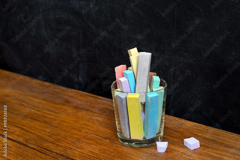 Obraz premium Glass of coloured chalk on desk in front of blackboard