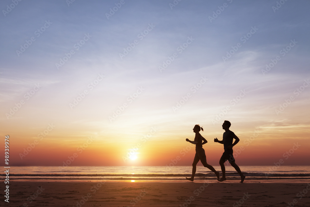 Silhouette of two runners running on the beach at sunset