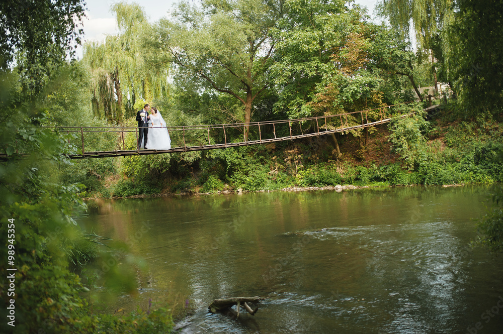 Just married couple on the suspension bridge over the river