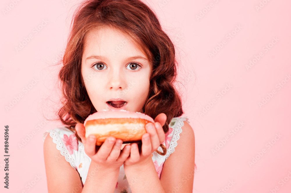 Cute little girl eating donut over pink. Looking at camera. Childhood. Cute little girl eating donut over pink. Looking at camera. Childhood.
