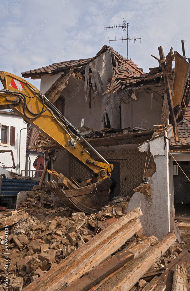 Fototapeta premium A large track hoe excavator tearing down an old house