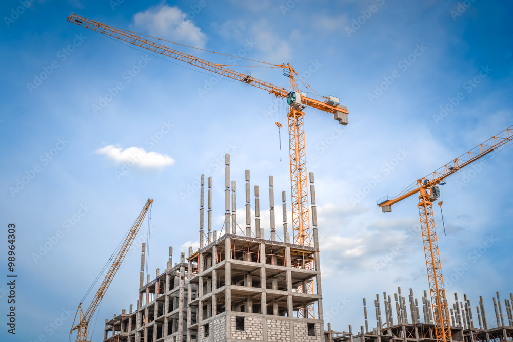Modern houses under construction and industrial construction cranes
