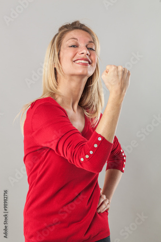 muscle concept - thrilled blond 20s woman with fist tight in the foreground showing her courage,studio shot