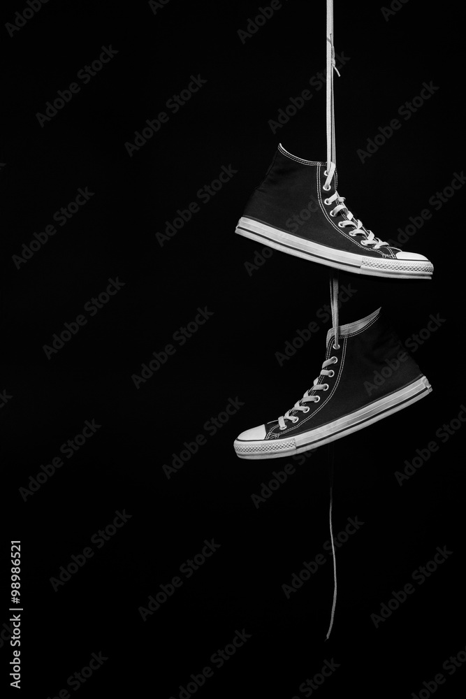 A pair of black and white sneakers hanging by their laces in front of a  black background foto de Stock | Adobe Stock