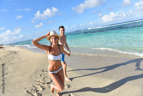 Slika na platnu CHeerful couple running on sandy beach in Caribbean island