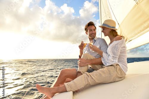 Romantic couple cheering on sailboat at sunset
