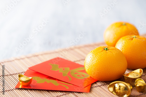Chinese New Year - Mandarin orange, gold sycee (Foreign text means wealth) and red packet (Foreign text means spring season) on white painted wood table