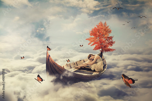 Young lonely beautiful woman drifting on a boat above clouds. Dreamy screensaver photo