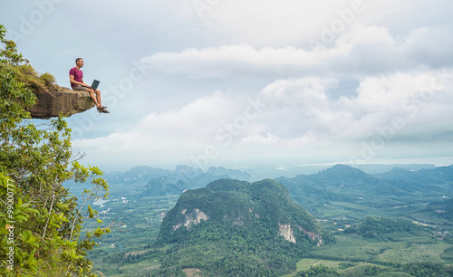 Man working with laptop sitting on the rocky mountain on beautiful scenic clif background. Thailand. Krabi . 