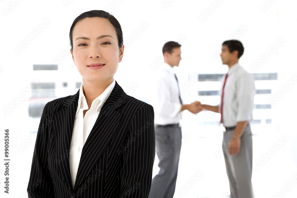 Successful Global Partnership - Asian woman looking at camera with partners shaking hands on background Successful Global Partnership - Asian woman looking at camera with partners shaking hands on background